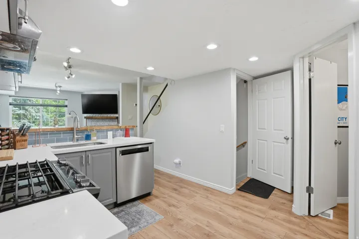 Modern kitchen featuring light gray cabinetry, stainless steel appliances, white countertops, and wood-finish flooring