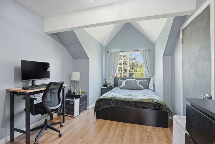 Room featuring sloped ceilings, wood-finish flooring, a window with exterior tree scenery, a built-in closet with a panel door, and painted walls