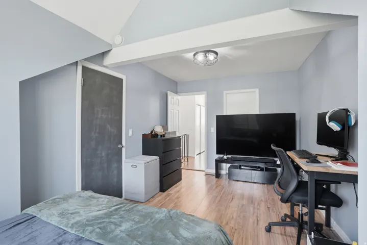 Bedroom featuring wood-finish flooring, light blue walls, and a white vaulted ceiling with exposed beams
