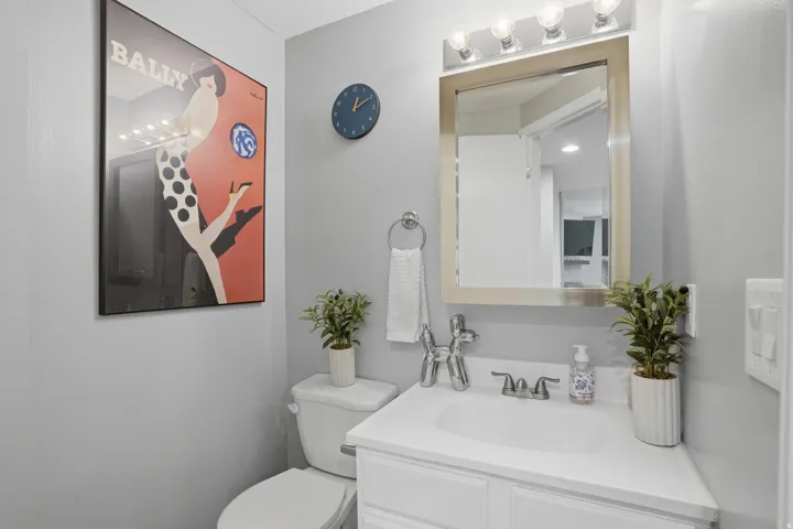 Compact bathroom featuring a white vanity with integrated sink, chrome faucet, and a framed mirror with overhead vanity lighting