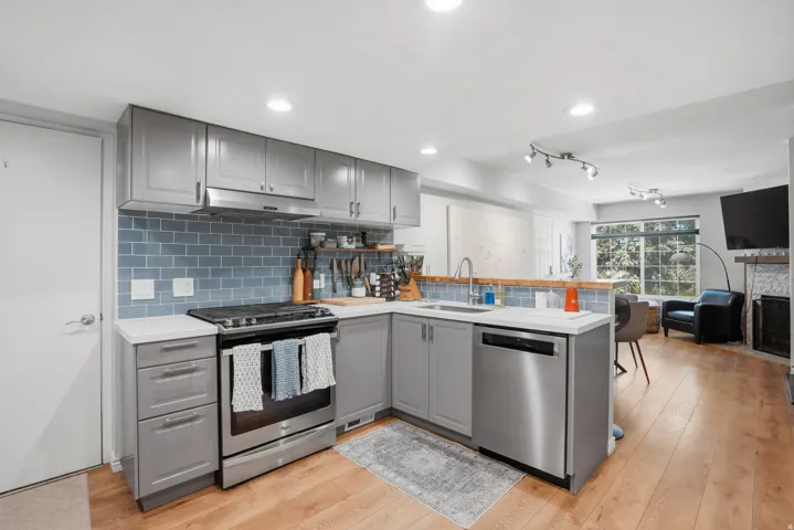 Modern kitchen featuring light gray cabinetry, stainless steel appliances, white countertops, and a blue subway tile backsplash