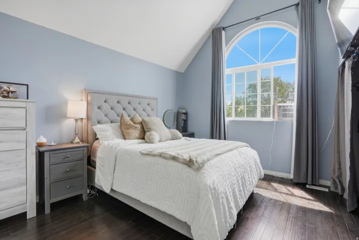 Vaulted ceiling featuring a large arched window with grid detailing, dark wood-finish flooring, and light blue wall color