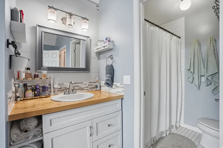 Bathroom featuring a white vanity with wood-finish countertop, undermount sink, and mosaic tile backsplash