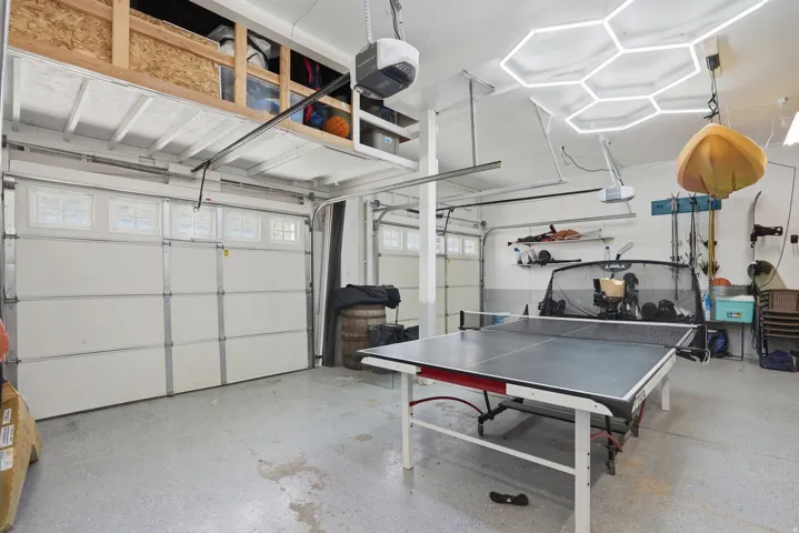 Spacious garage featuring two overhead doors with window accents, an epoxy-finished concrete floor, and integrated overhead storage shelving