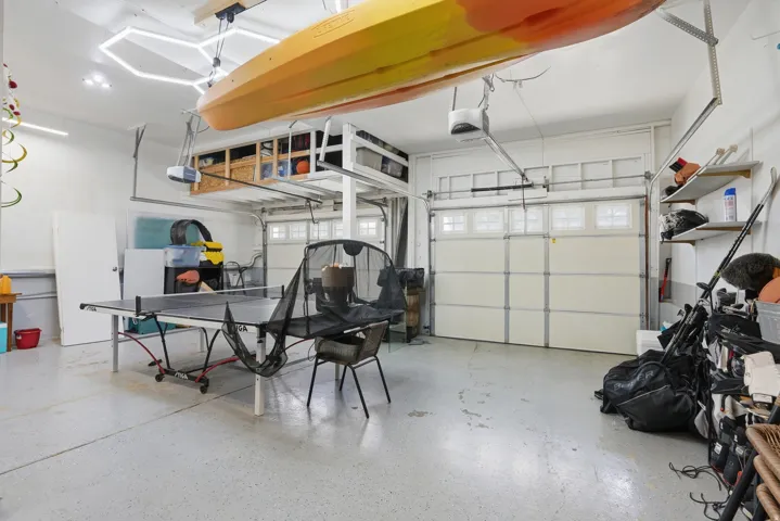 Spacious garage featuring a durable epoxy floor coating, two overhead garage doors with frosted window panels, built-in shelving, and recessed lighting
