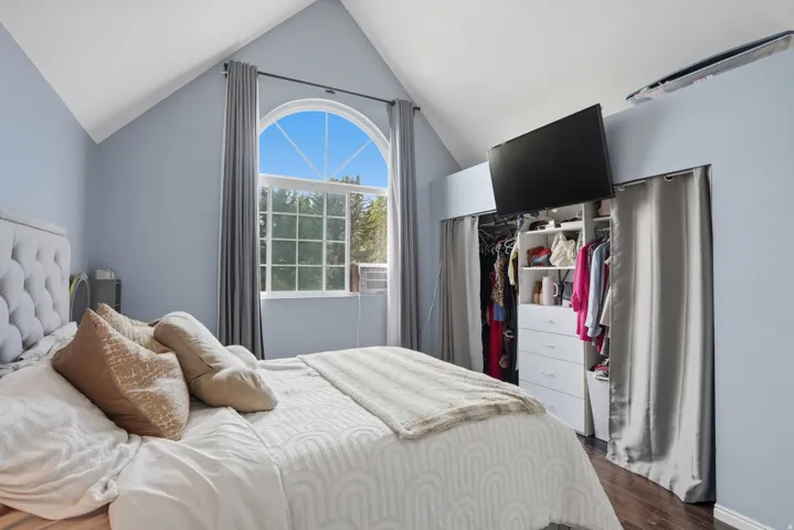 Vaulted ceiling bedroom featuring an arched window, wood-finish flooring, and built-in closet organization system