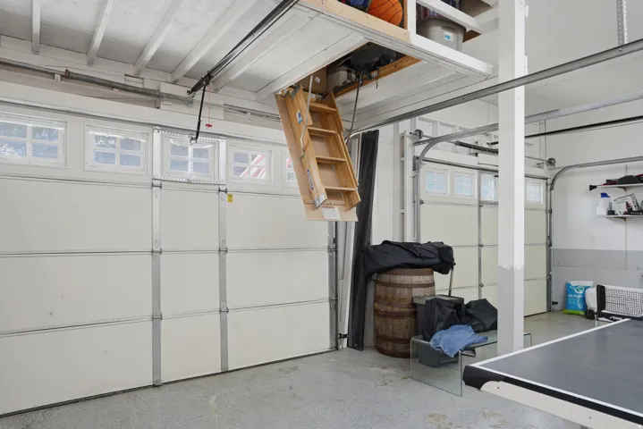 Spacious garage featuring a finished ceiling with exposed rafters, two overhead garage doors with frosted window panels, and a pull-down attic access ladder