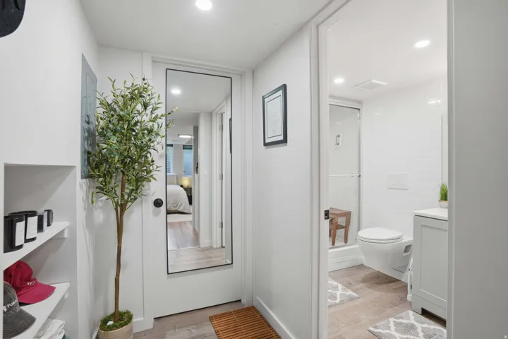 Bathroom entry featuring a wall-mounted toilet, glass-enclosed shower, single vanity with white countertop, and wood-finish flooring