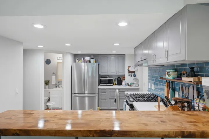 Kitchen featuring wood-finish countertop, blue subway tile backsplash, stainless steel appliances, recessed lighting, and gray cabinetry