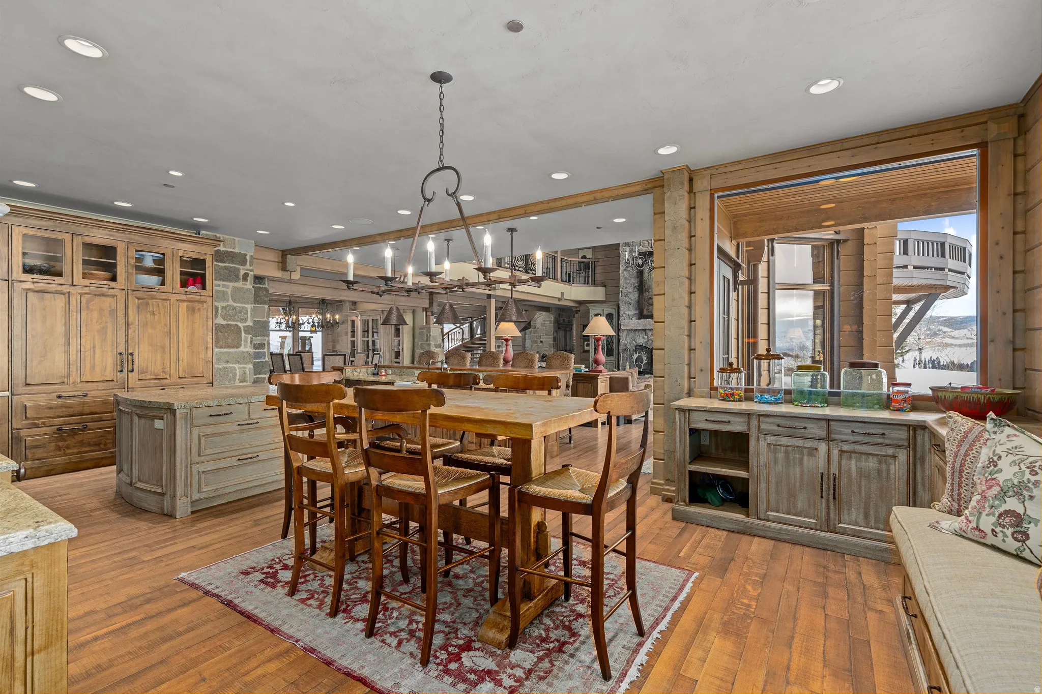 Open-concept kitchen and dining space featuring wood-finish flooring, a stone accent wall, an elongated dining table with seating, recessed lighting, and a built-in window bench