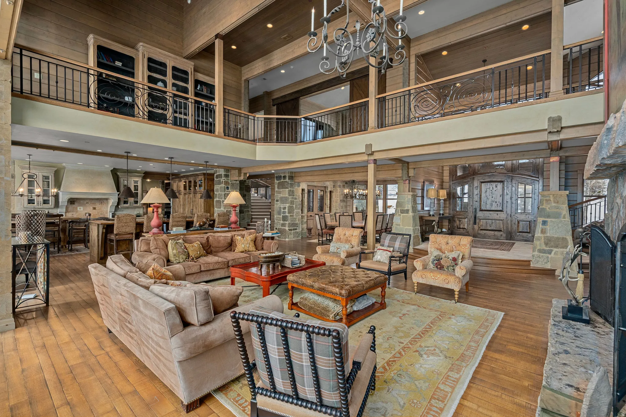 Two-story living area featuring wood-finish flooring, a stone-clad fireplace, and a wrought iron chandelier
