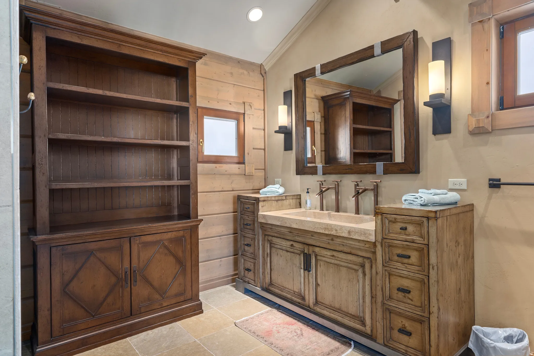 Stone tile flooring featuring a dual vanity with integrated stone sinks and wall-mounted bronze-finish faucets
