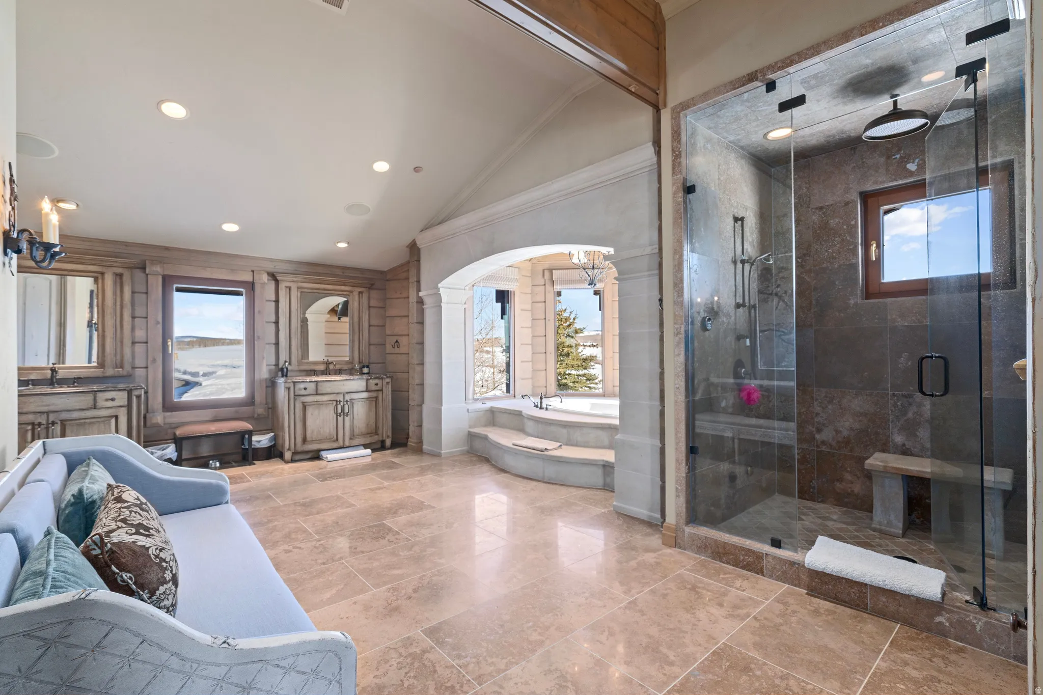 Spacious bathroom featuring stone tile flooring, a large glass-enclosed shower with a built-in bench, and a jetted soaking tub