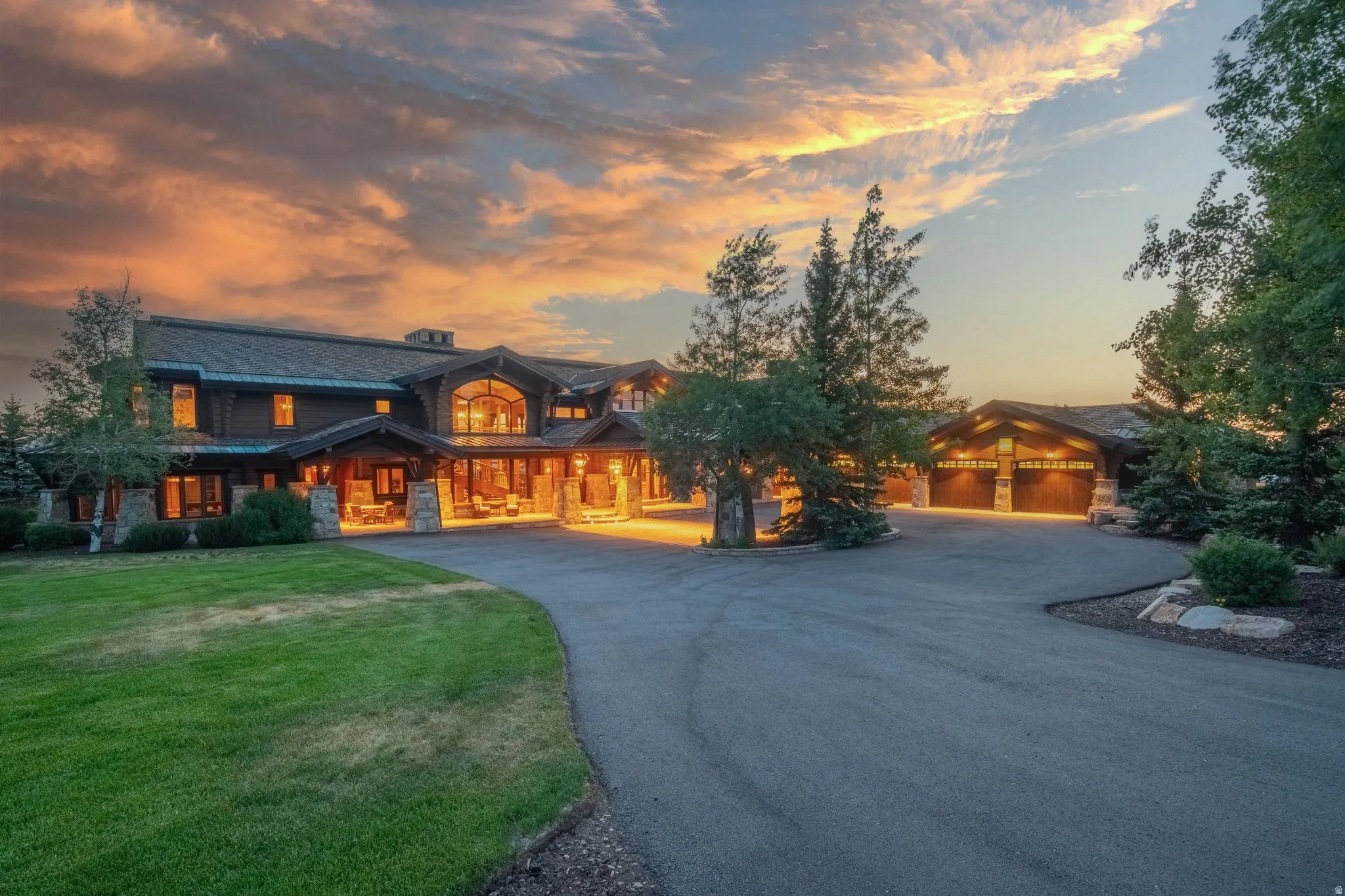 Spacious residential property featuring a large asphalt driveway, a multi-car garage, manicured lawns, mature trees, and stone architectural accents
