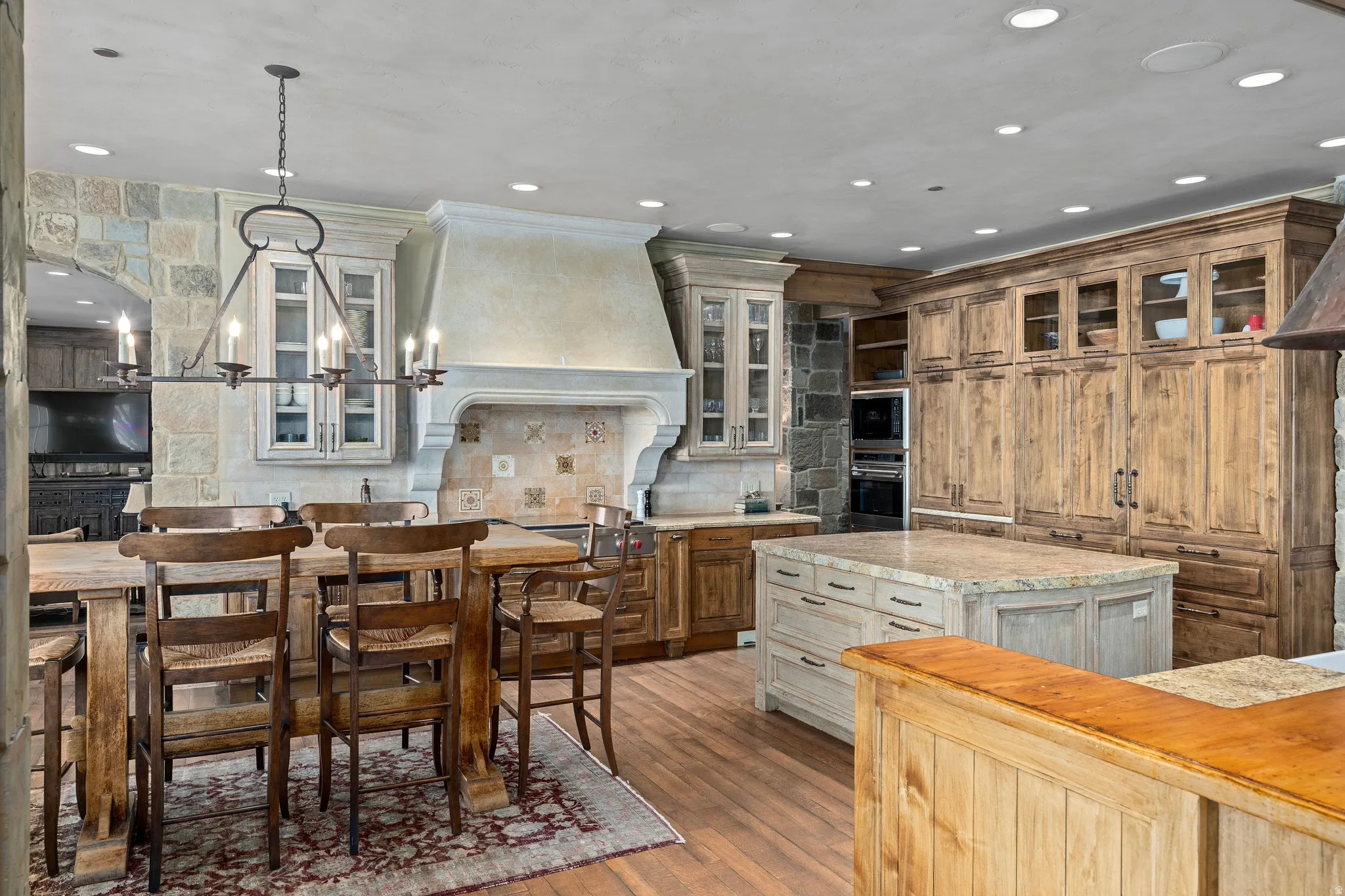 Spacious kitchen featuring a large central island, extensive light wood cabinetry, stone accent walls, recessed lighting, and a decorative range hood