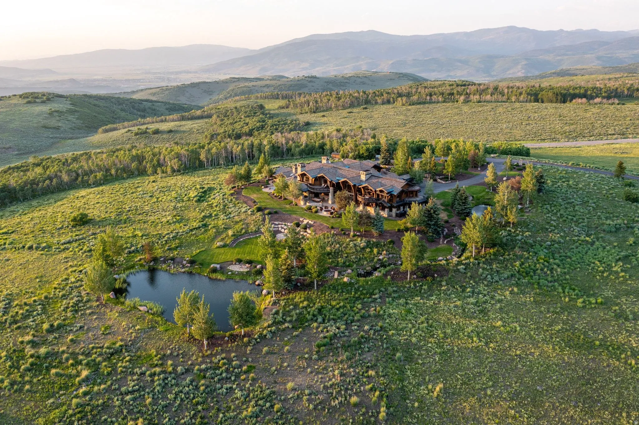 Expansive property featuring a large residence with multiple gables, surrounding mature trees, and a private pond