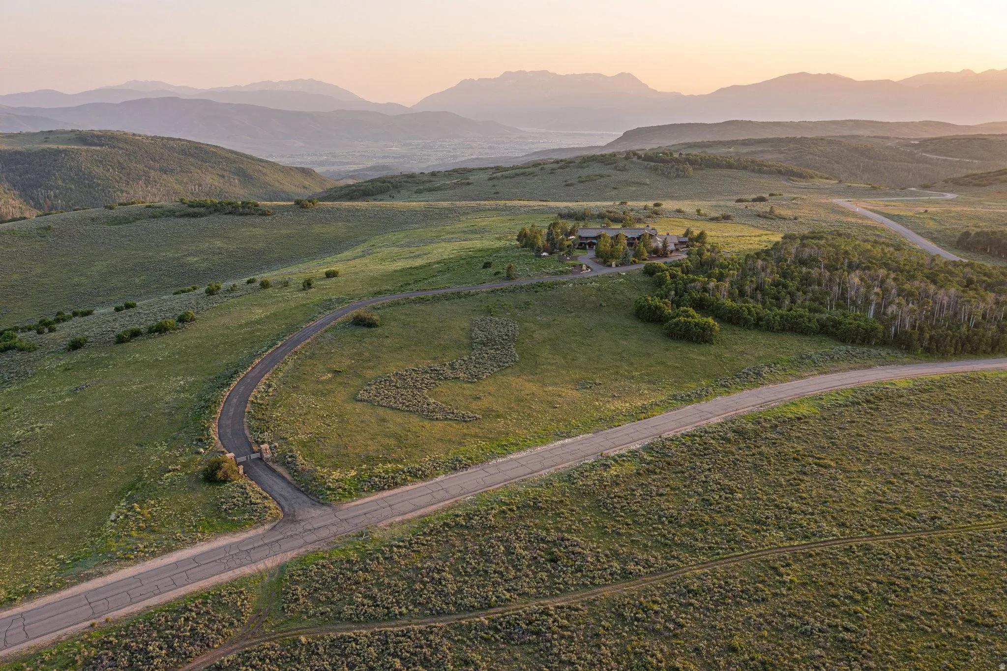 Expansive rural property featuring a winding paved road, lush green hills, and distant mountain ranges