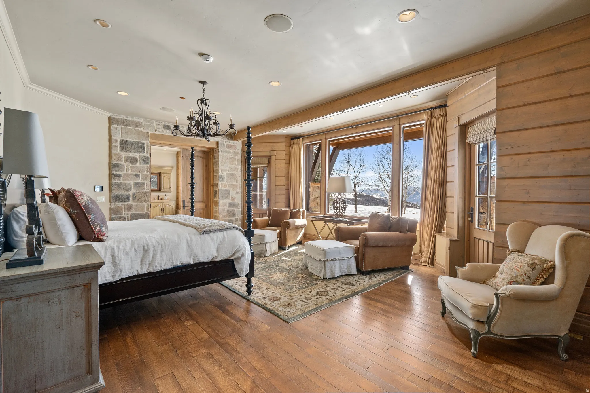 Expansive room featuring rich wood-finish flooring, a full stone accent wall, and a large window wall showcasing the exterior landscape