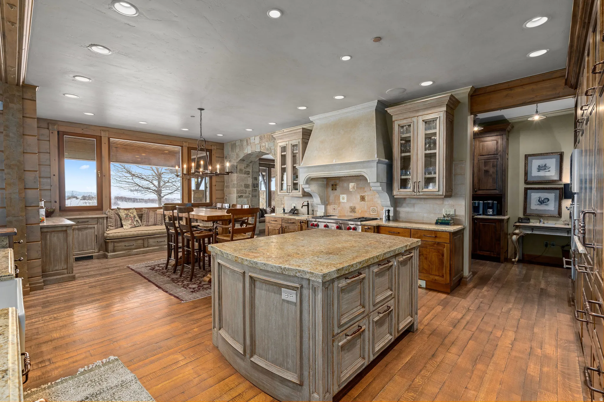 Gourmet kitchen featuring a large stone-finish island with granite countertop, wood-finish flooring, custom cabinetry, recessed lighting, and a built-in banquette