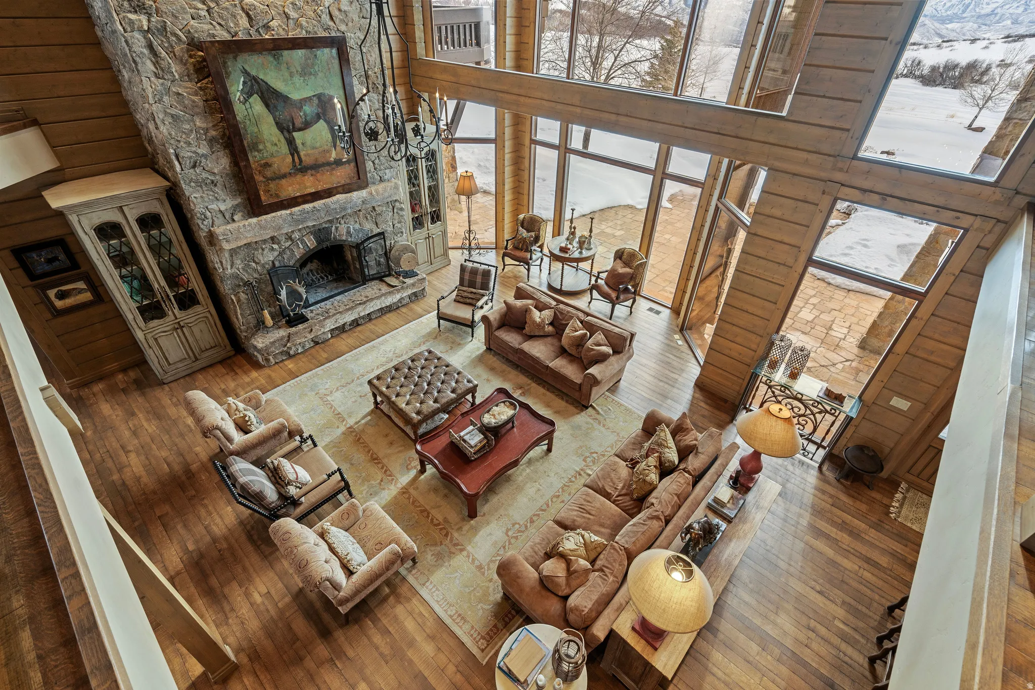 Two-story living area featuring a stone fireplace, wood-finish flooring, and expansive windows