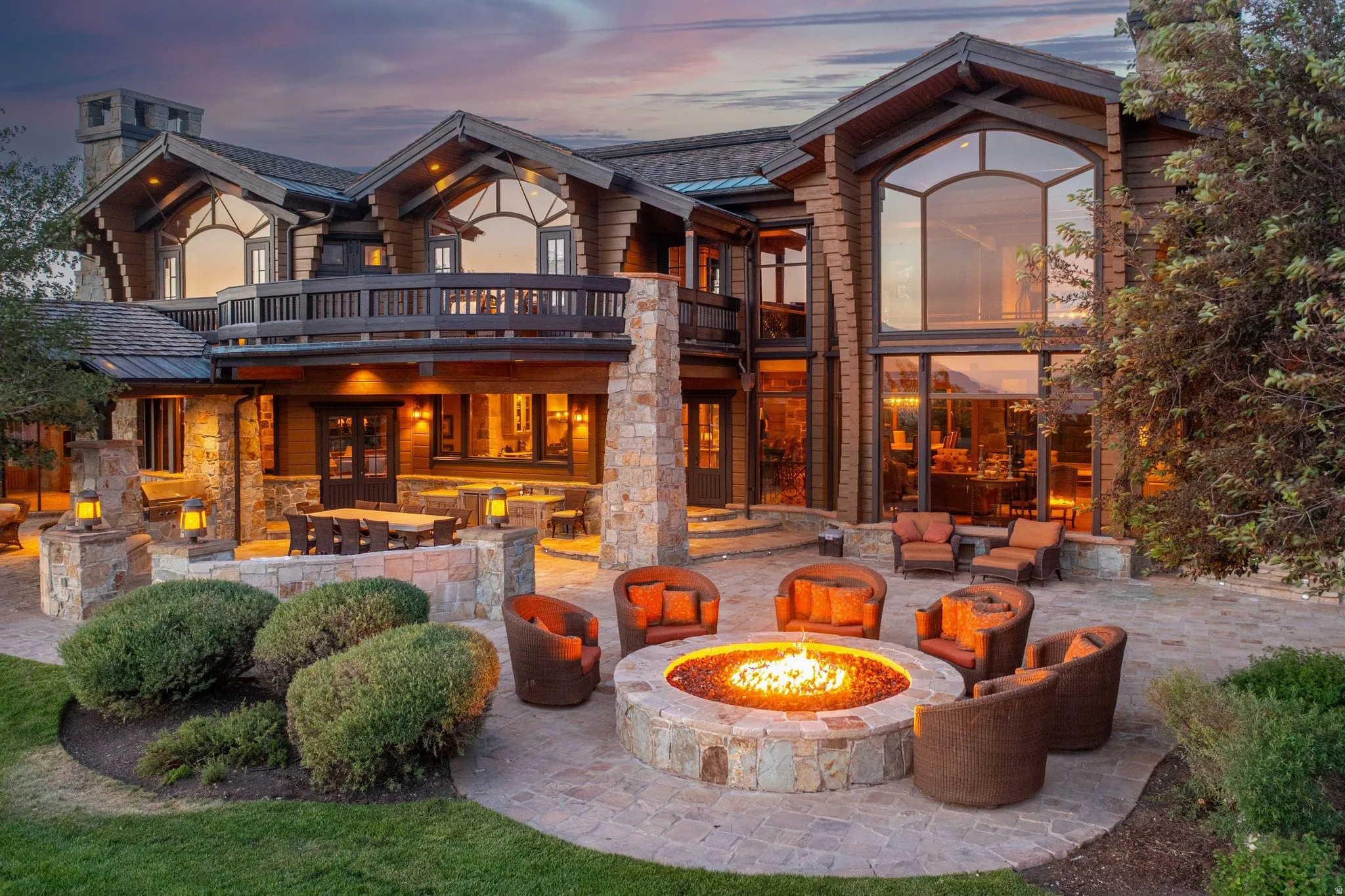Expansive stone patio featuring a built-in fire pit, multiple seating areas, and architectural lighting