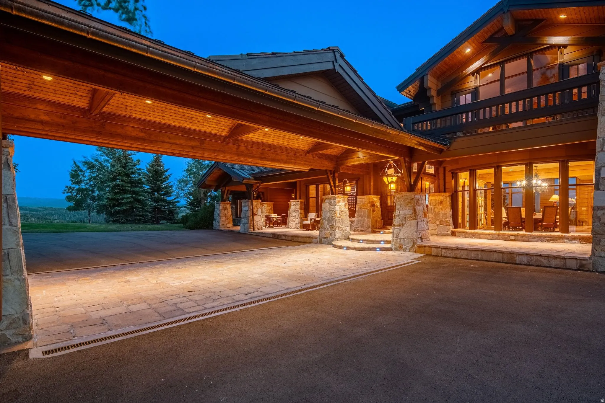 Stone and timber porte-cochère with recessed lighting and a paver stone drive