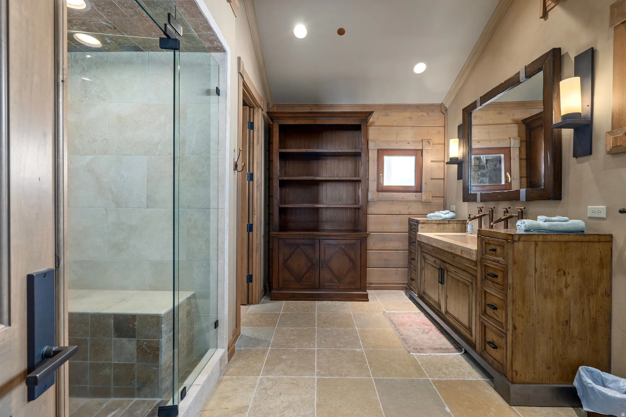 Bathroom featuring a glass-enclosed shower with tile surround and built-in bench, a dual vanity with wood-finish cabinetry, a large framed mirror, and recessed lighting