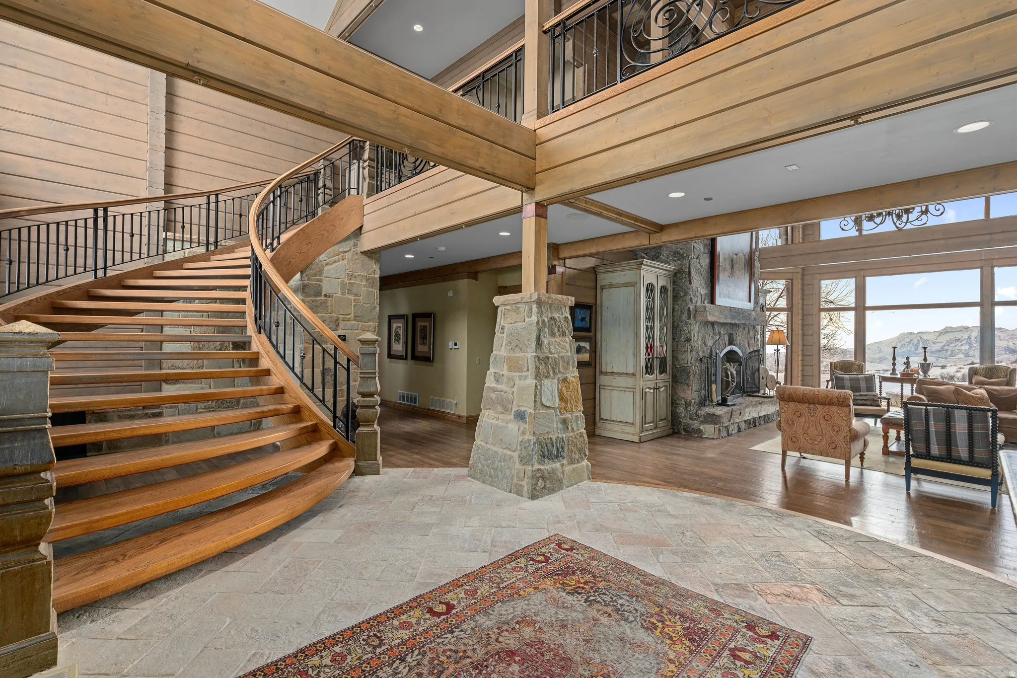 Grand entryway featuring a curved wood staircase with wrought iron balusters, stone column, and stone-clad fireplace