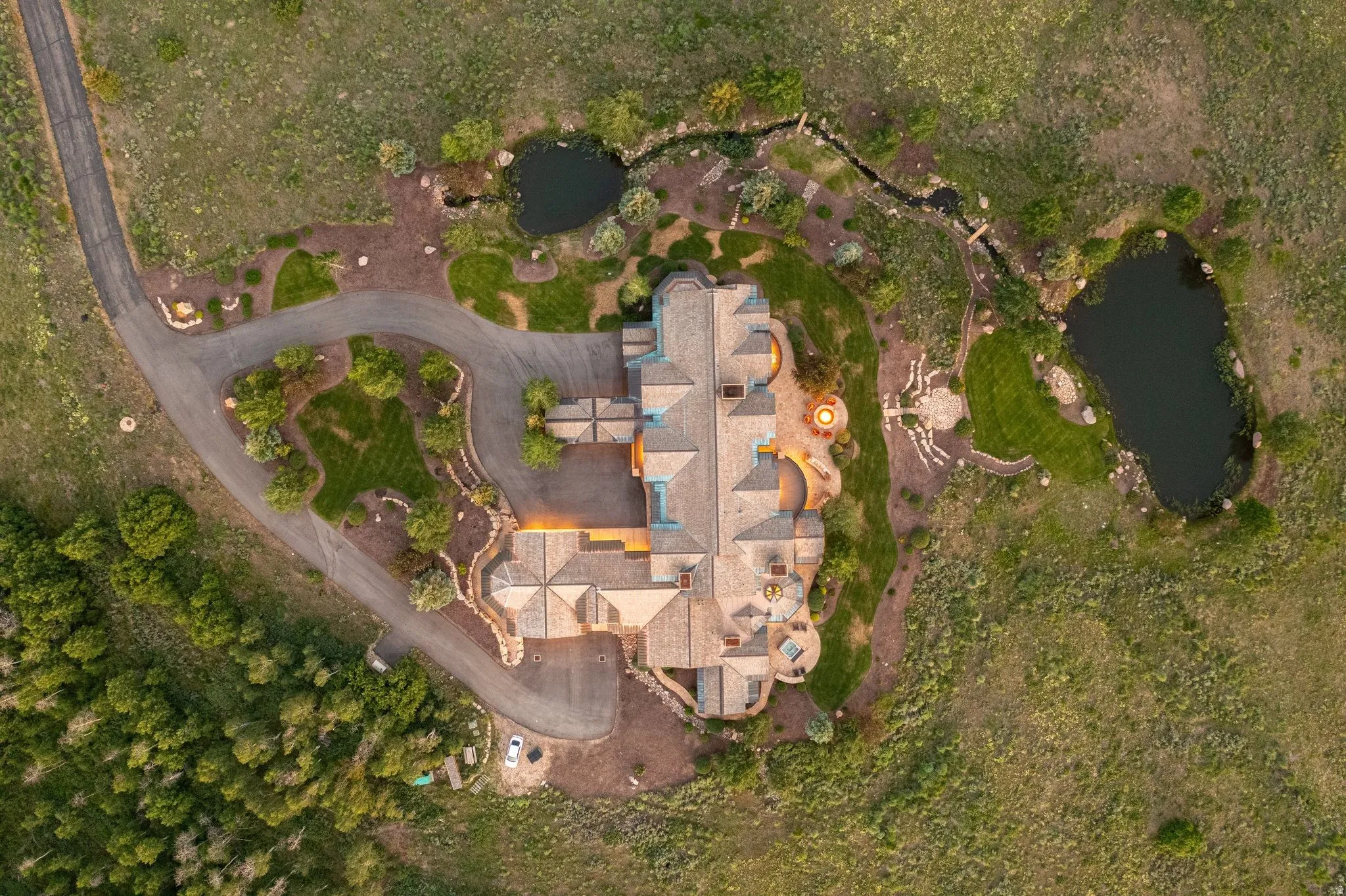 Expansive estate featuring a multi-level roofline, extensive paved driveway, two distinct ponds, a meandering stream, and landscaped grounds