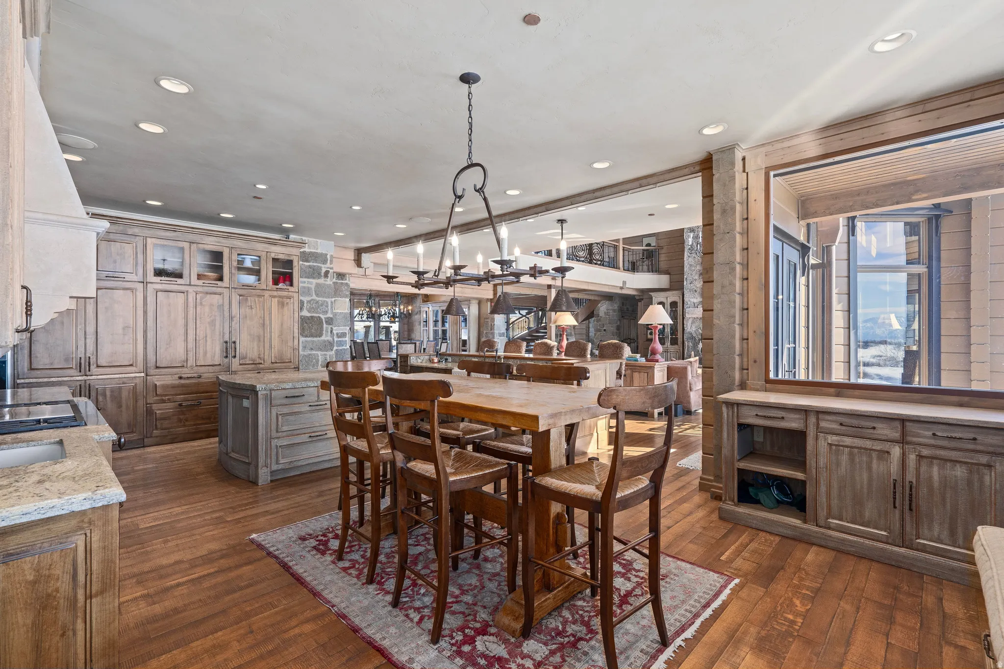 Spacious kitchen and dining area featuring wood-finish flooring, a stone accent wall, and built-in cabinetry with glass inserts