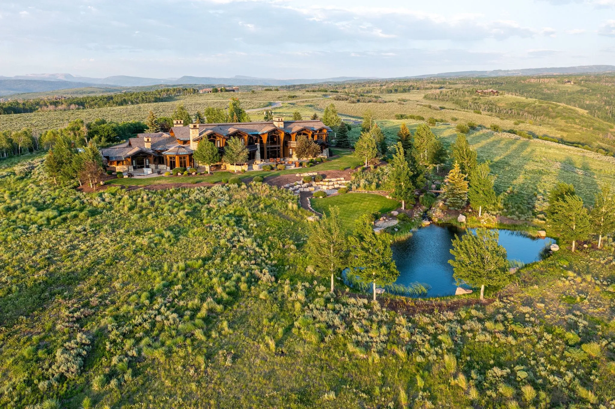 Expansive estate featuring a large main residence, multiple chimneys, a private pond, mature trees, and a surrounding natural landscape