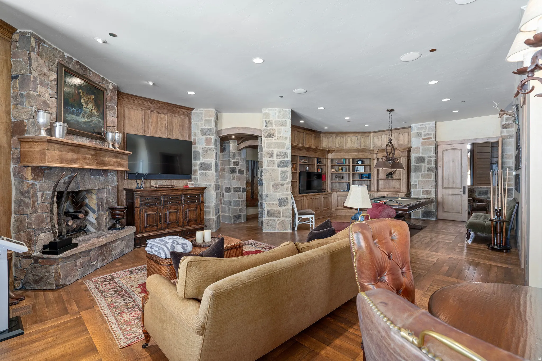 Stone-clad fireplace with a substantial hearth and wood mantle, complemented by recessed lighting and wood-finish flooring