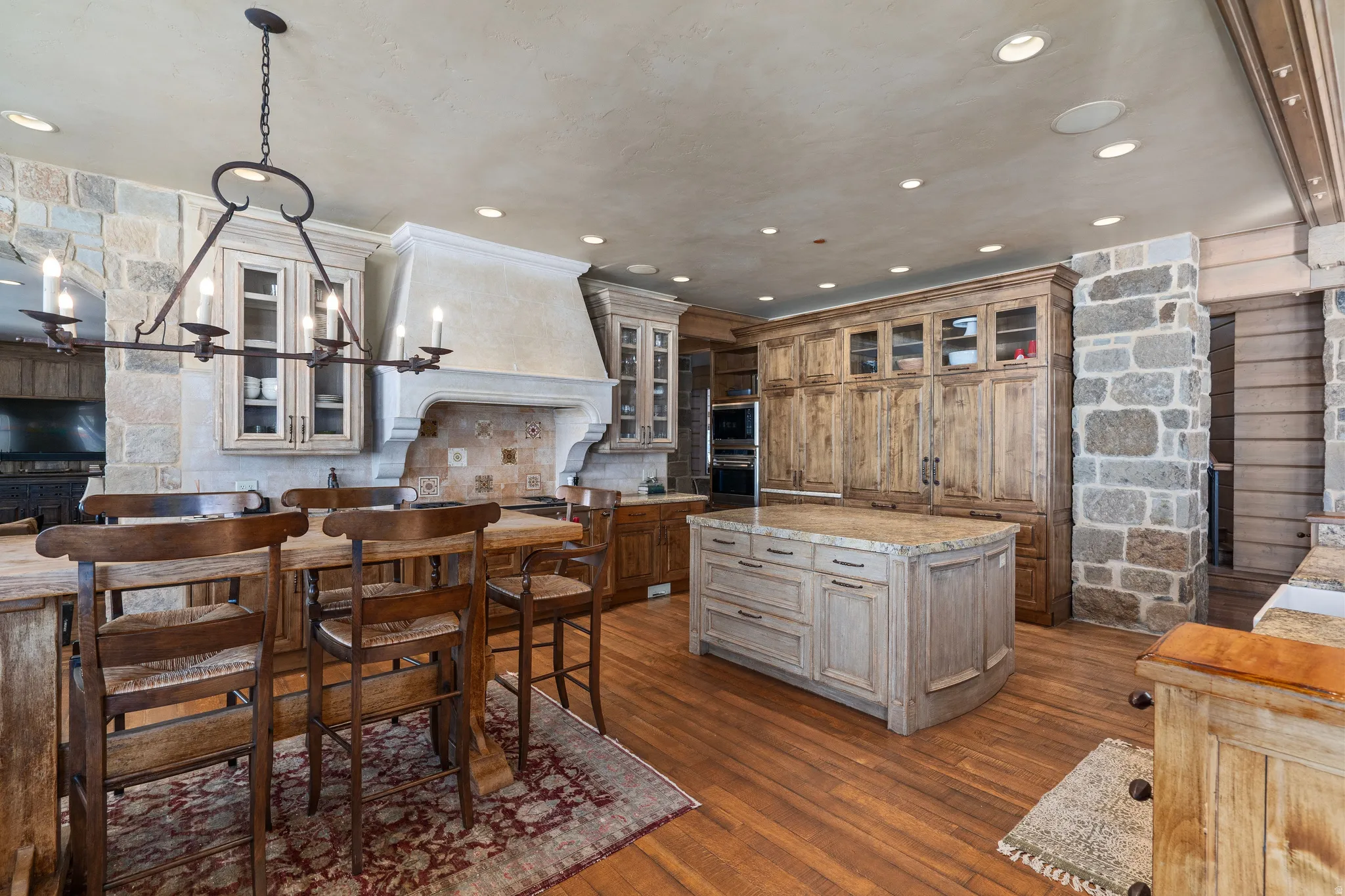 Spacious kitchen featuring stone accent walls, wood-finish flooring, and a large center island with a stone countertop