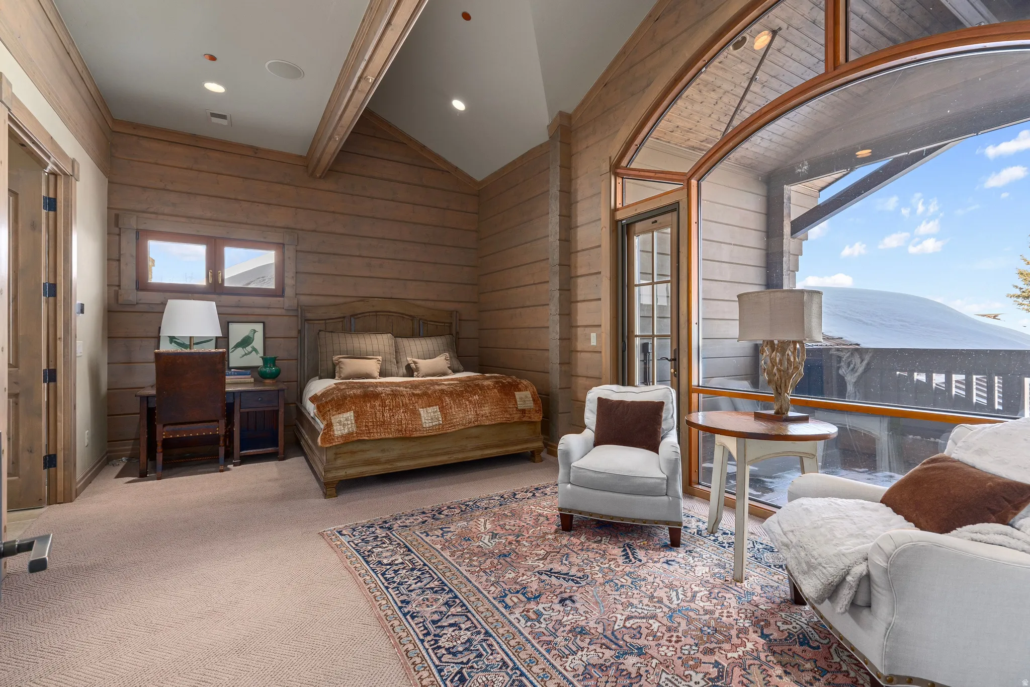 Vaulted ceilings with exposed wood beams, expansive wood-paneled walls, and a large arched window with a glass door