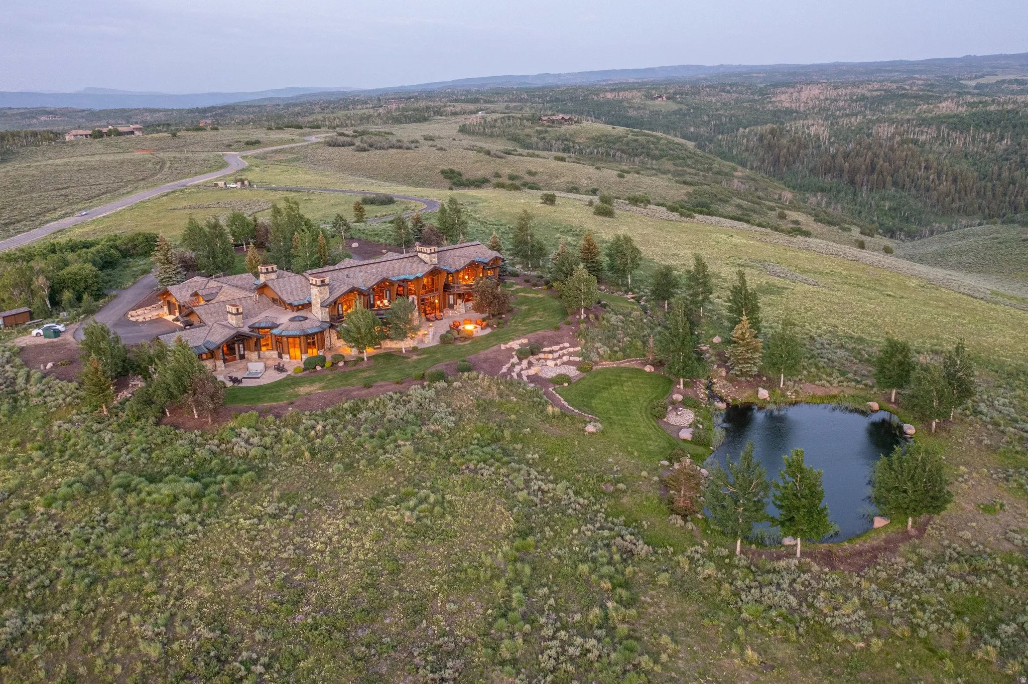 Expansive estate with a large main residence, private pond, and natural landscaping surrounded by rolling hills
