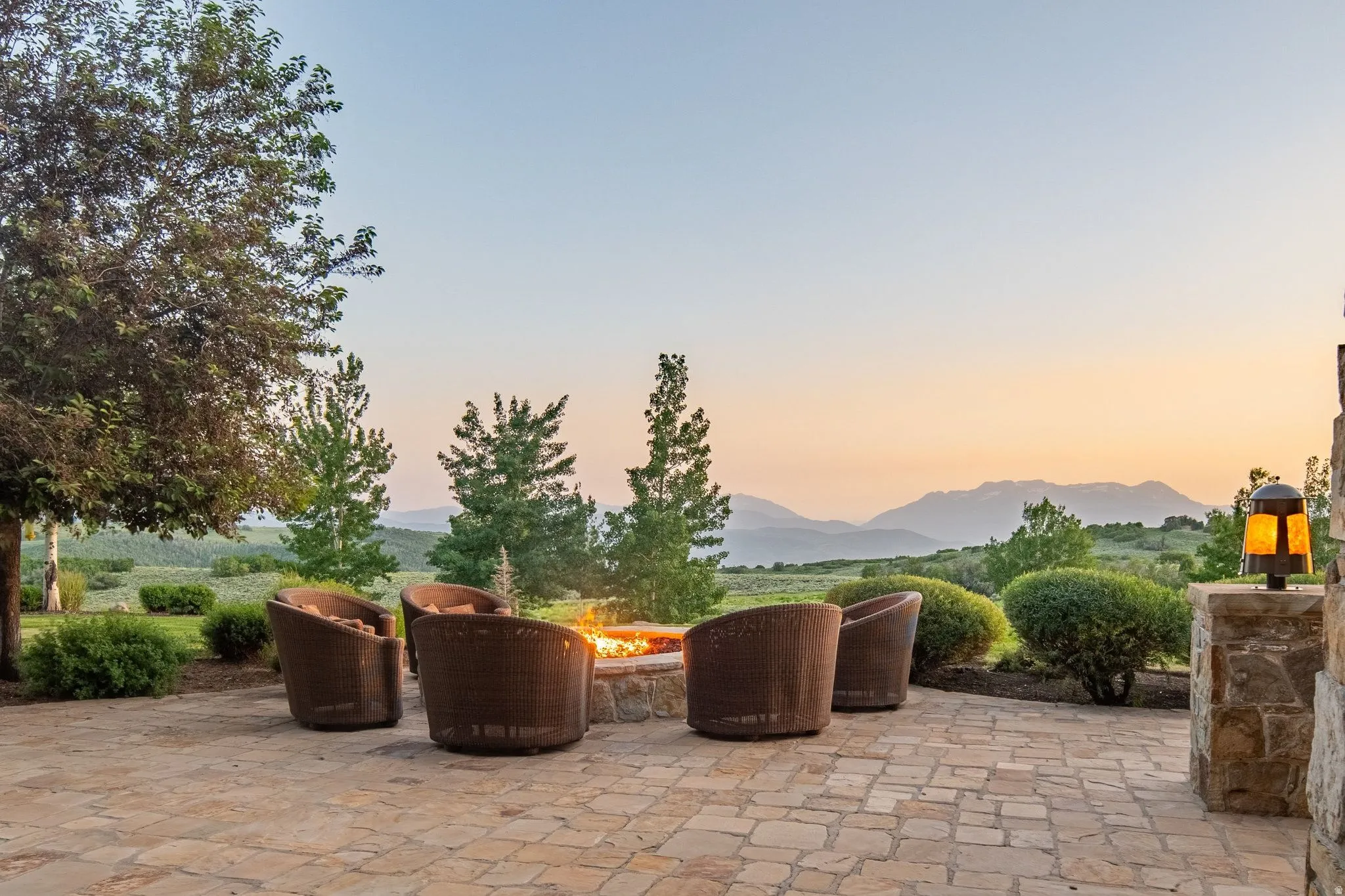Stone patio featuring a built-in fire pit, stone accent column with a sconce, and distant mountain scenery