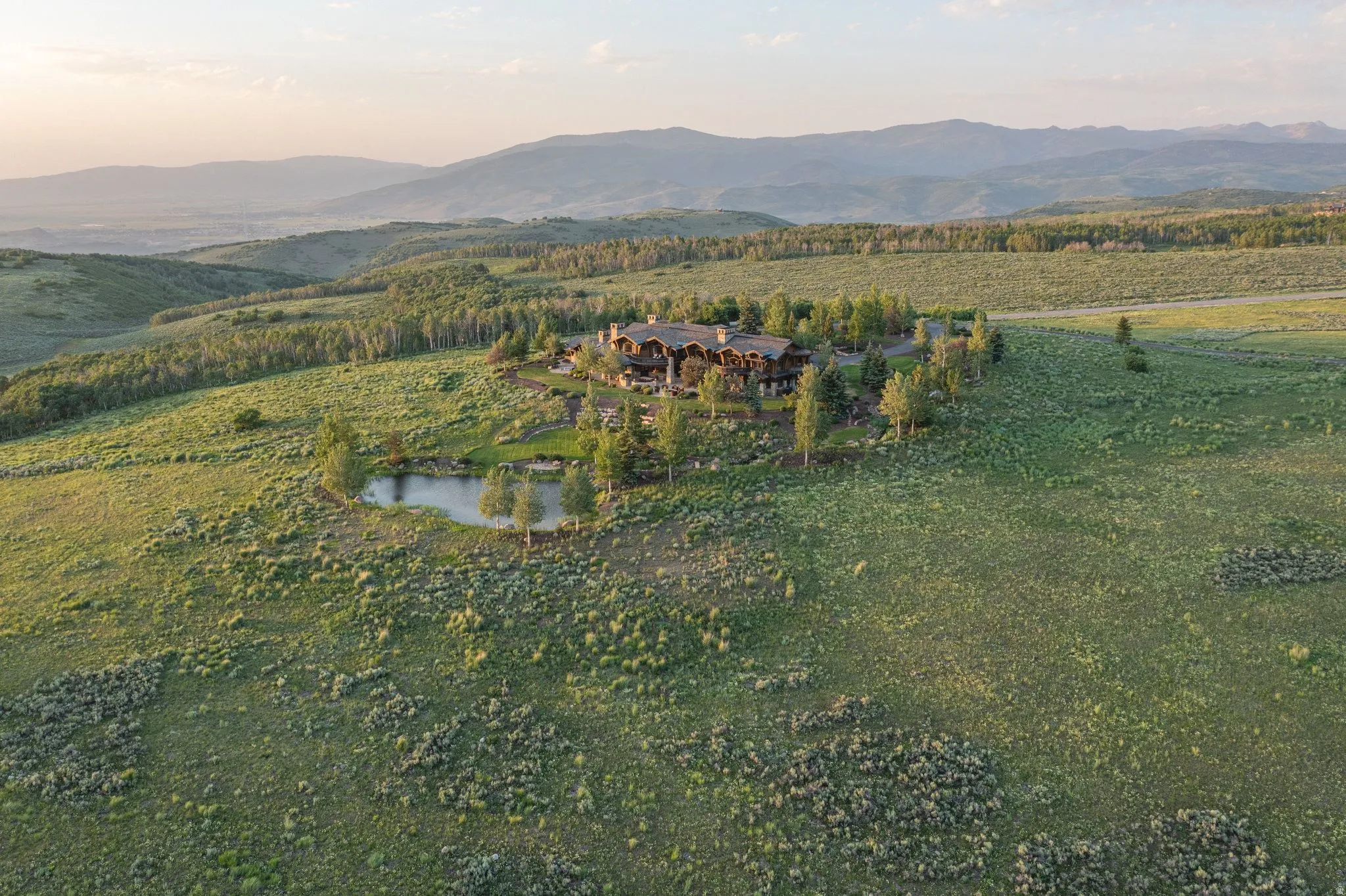 Expansive property featuring a large residence, a private pond, and mature evergreen trees, set against a backdrop of rolling hills and distant mountains