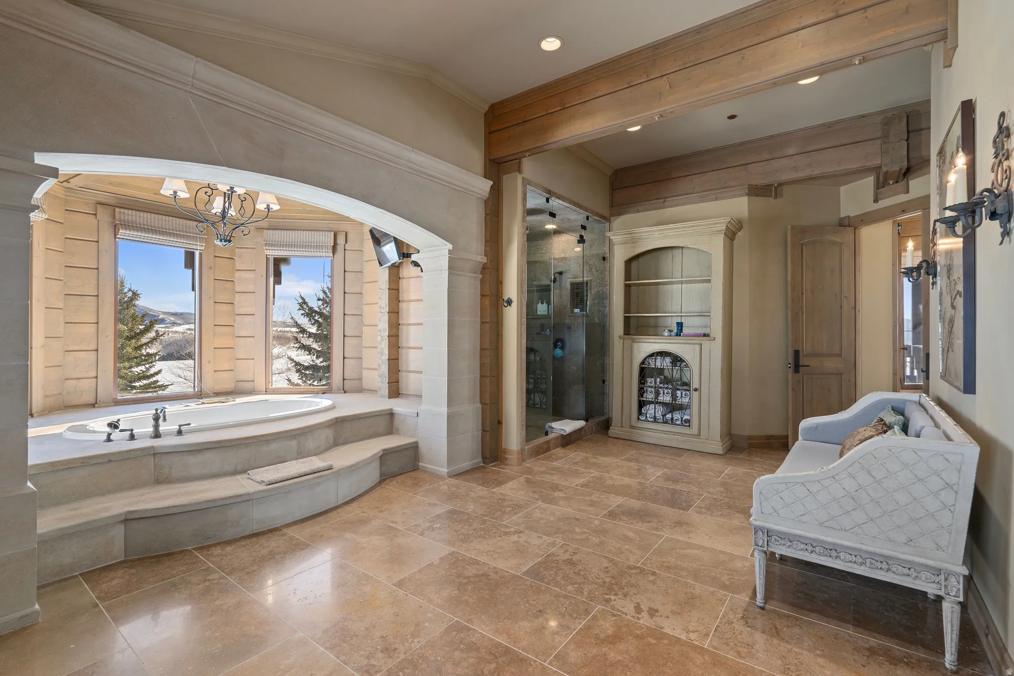 Spacious bathroom featuring large format stone tile flooring, a sunken soaking tub with stepped surround, and a glass-enclosed shower