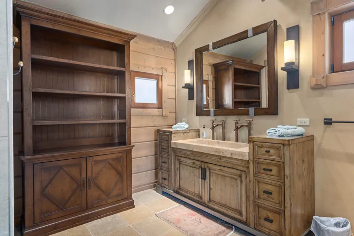 Stone tile flooring featuring a dual vanity with integrated stone sinks and wall-mounted bronze-finish faucets