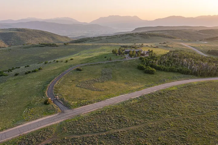 Expansive rural property featuring a winding paved road, lush green hills, and distant mountain ranges