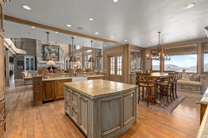 Expansive kitchen and dining area featuring wood-finish flooring, two large kitchen islands with stone countertops, a farmhouse sink, and panoramic windows showcasing mountain scenery