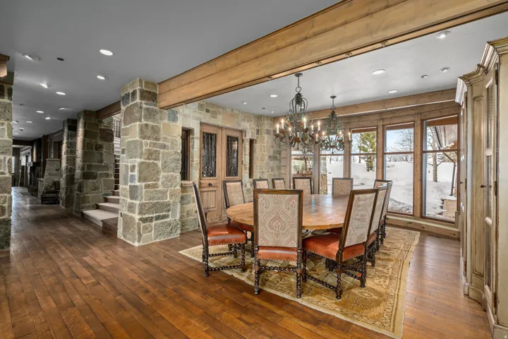 Spacious dining area featuring wood-finish flooring, stone accent walls, exposed ceiling beams, and a prominent chandelier