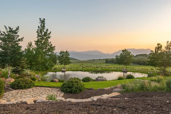 Expansive pond with surrounding natural landscape, mature trees, a stone patio, and distant mountain ranges