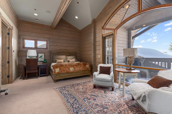 Vaulted ceilings with exposed wood beams, expansive wood-paneled walls, and a large arched window with a glass door