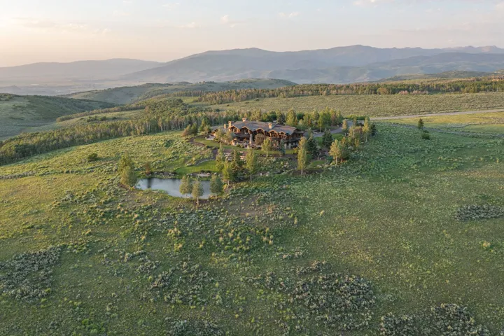 Expansive property featuring a large residence, a private pond, and mature evergreen trees, set against a backdrop of rolling hills and distant mountains