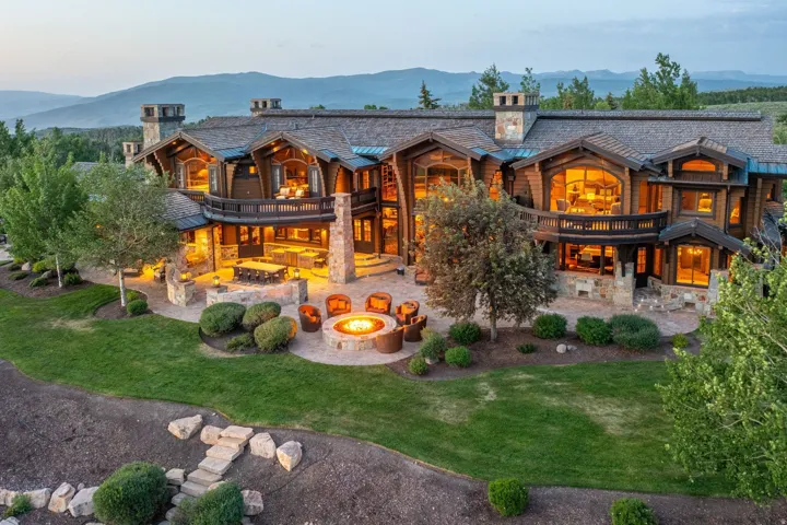 Wood-sided estate featuring multiple balconies, stone chimneys, and expansive windows