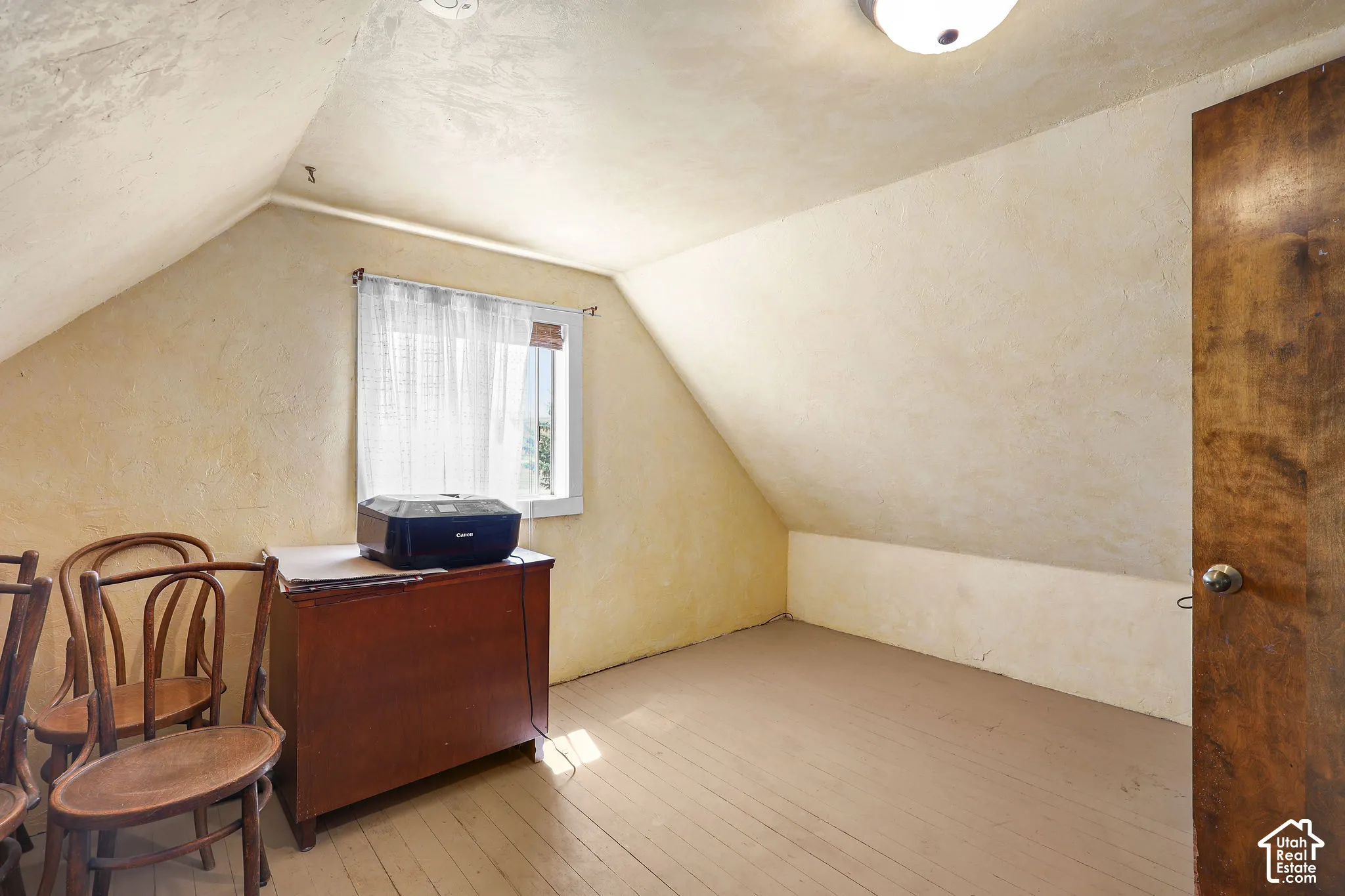 Attic room featuring sloped ceilings, painted wood-finish flooring, a single window with curtain rod, and a solid wood door