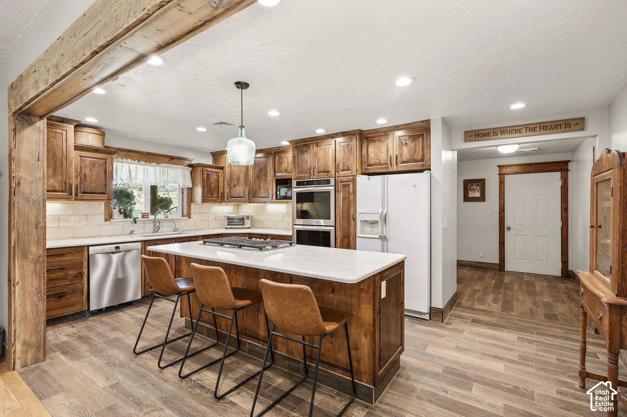 Kitchen with wood-finish cabinetry, stainless steel appliances, and an expansive island featuring a white countertop