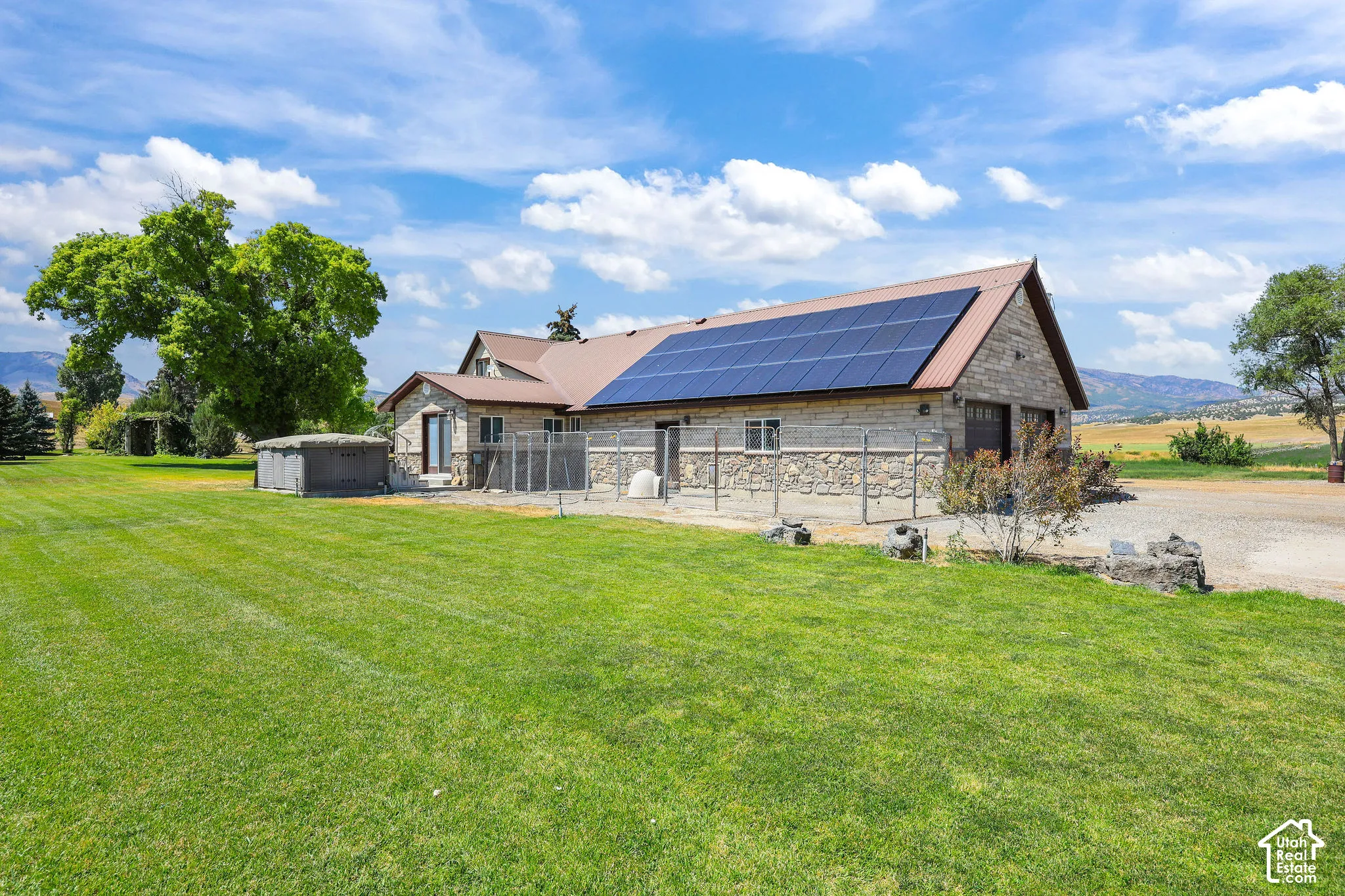 Stone exterior residence featuring a metal roof with integrated solar panels, a two-car garage, and an expansive manicured lawn
