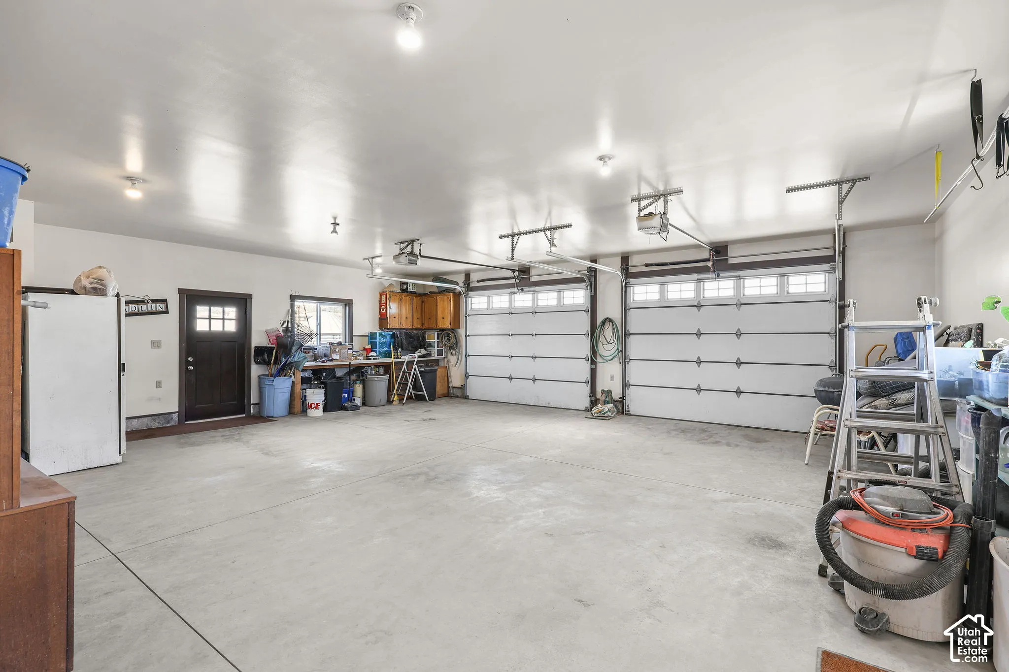 Spacious three-car garage featuring a concrete floor, two white paneled garage doors with upper window inserts, and an additional side entry door with glass panes
